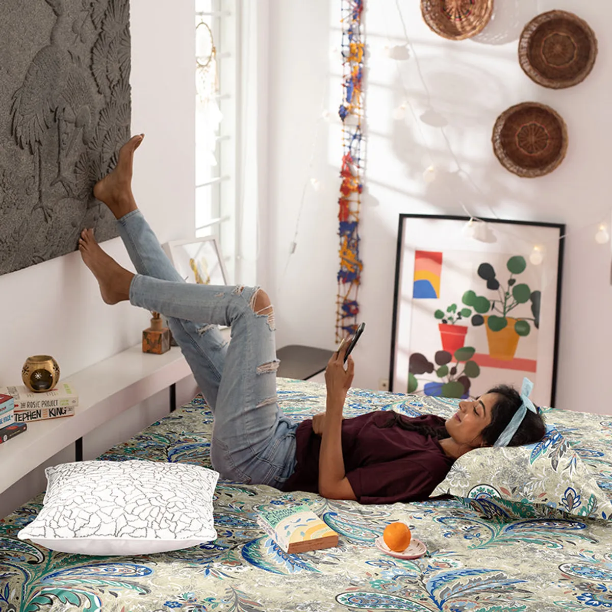 Woman reclining on a paisley comforter while reading on a bed