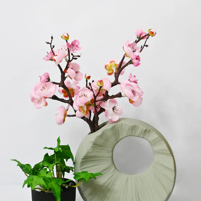 Pink artificial blossom arrangement beside a green indoor plant