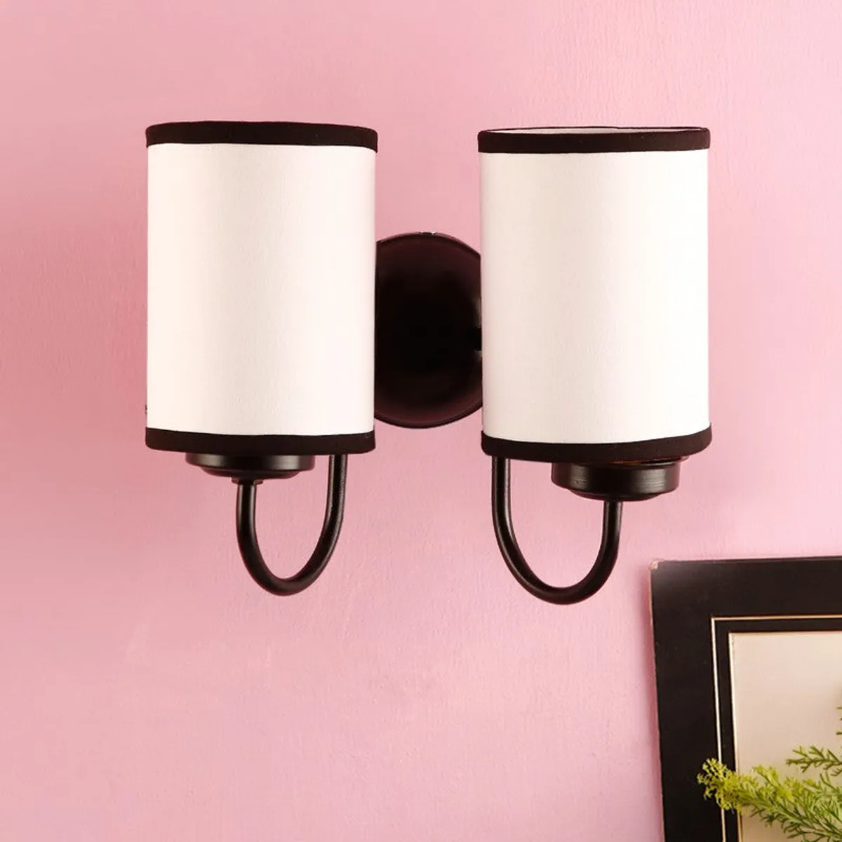 Front view of white dual wall lamp with dark iron arms against a pink wall