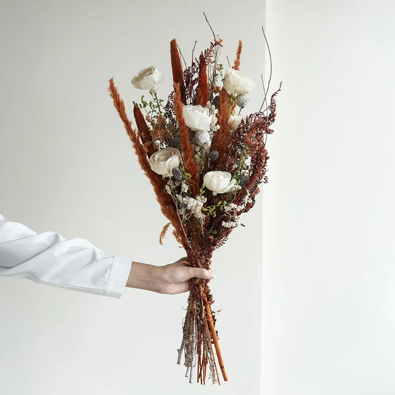 Hand holding a dried flower bouquet with white blooms and earthy foliage