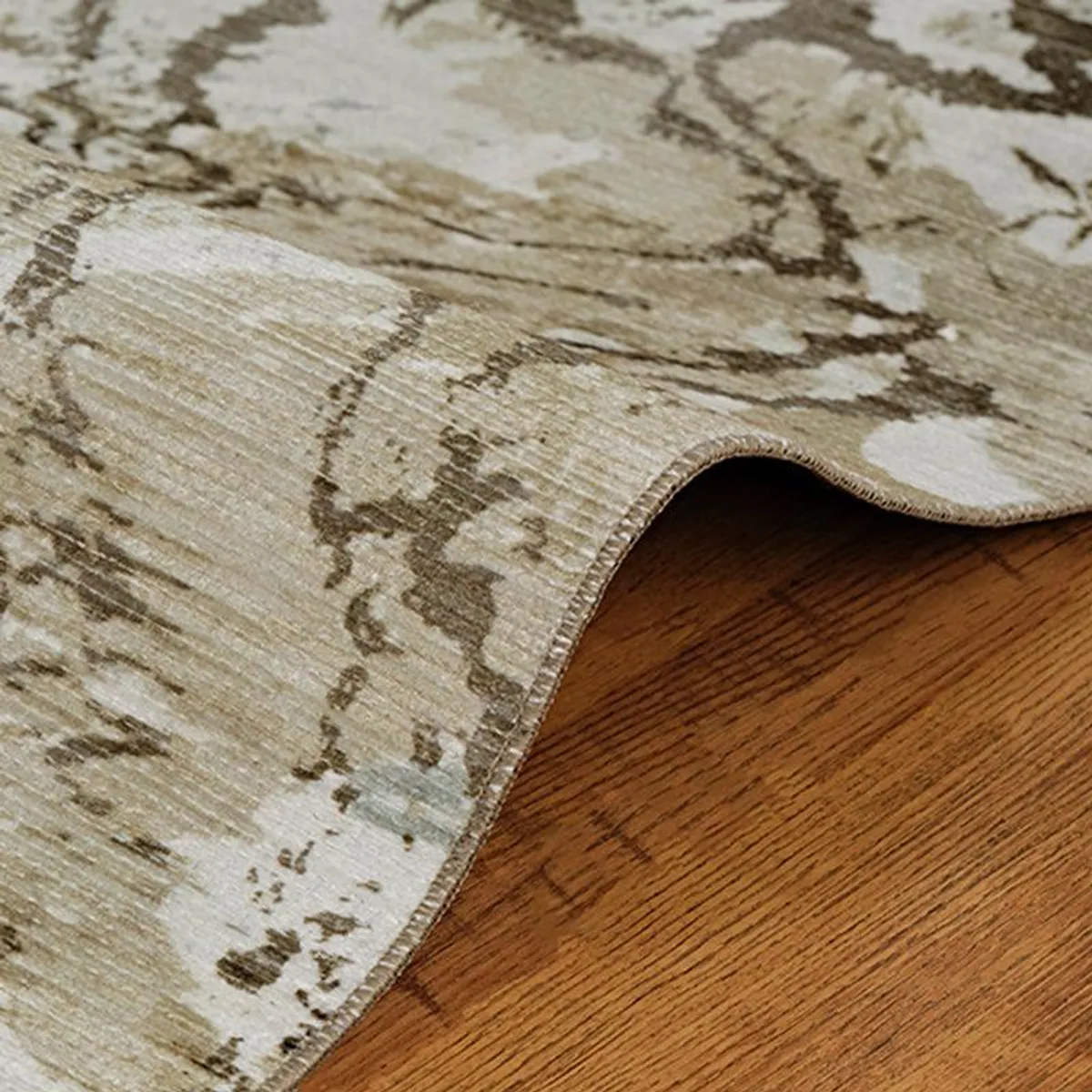 Rolled edge of the beige and green abstract carpet on a wooden floor
