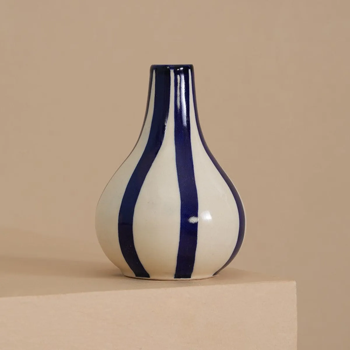 Blue and white striped ceramic vase placed on a beige pedestal