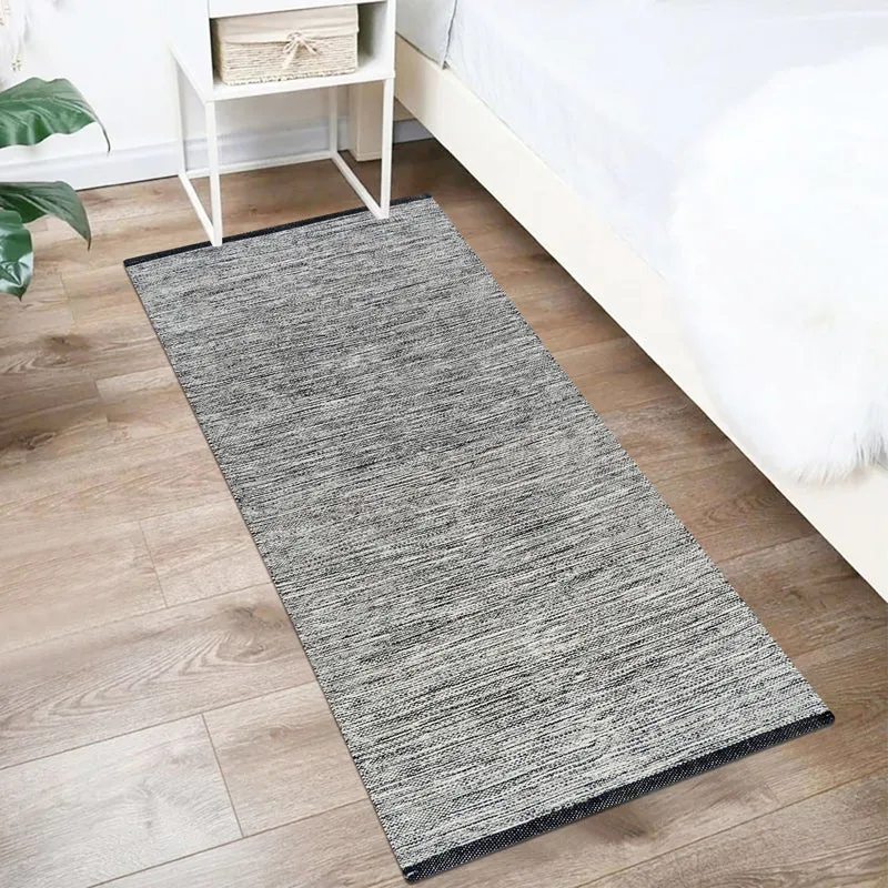 Charcoal-grey runner rug placed beside a bed on a wooden floor.