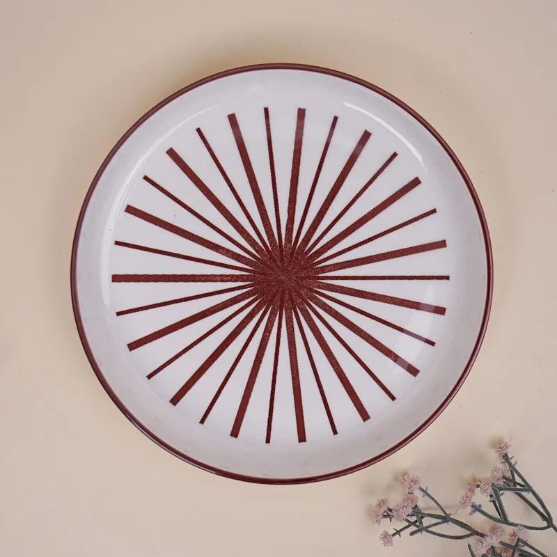 Top view of a white plate with maroon starburst design