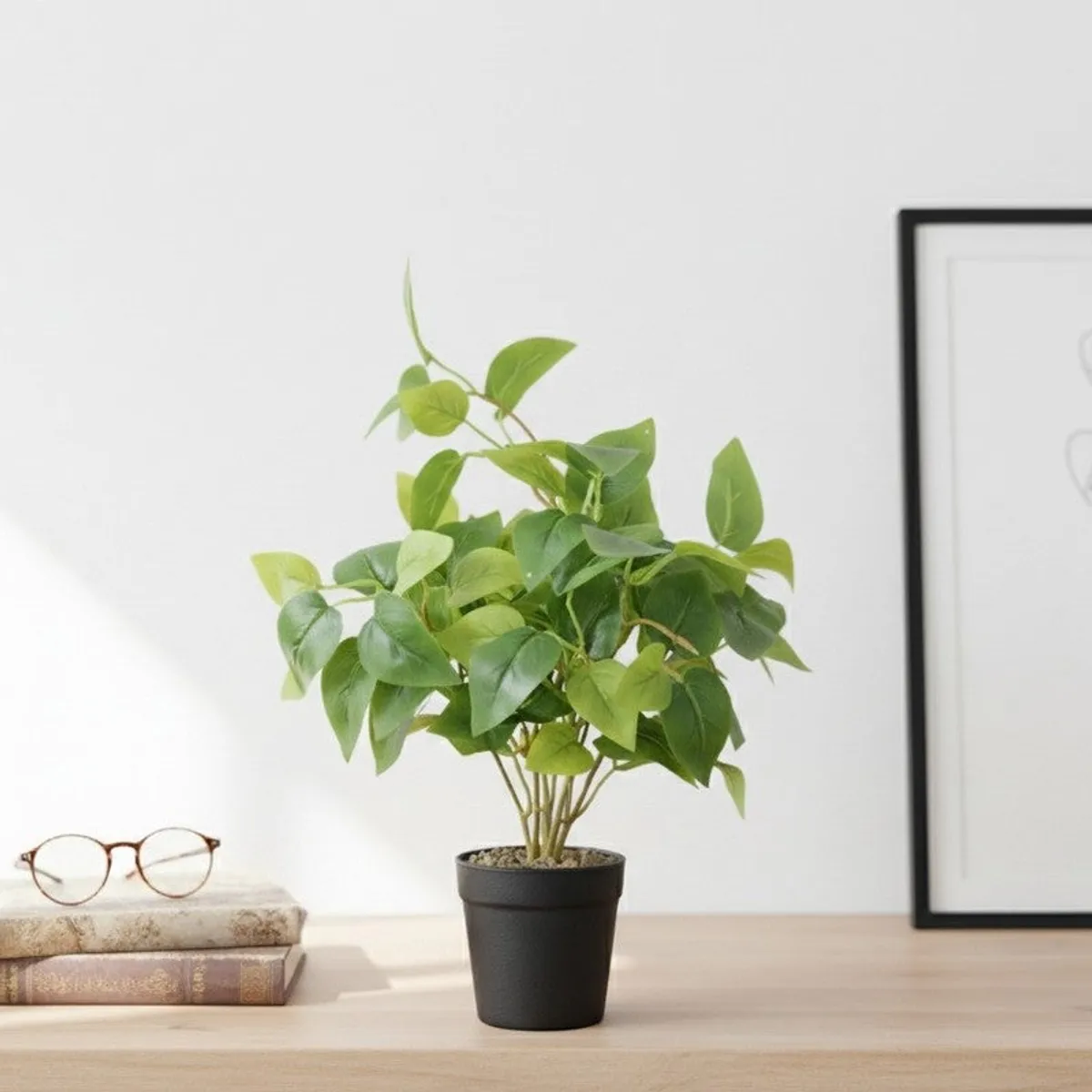Potted artificial green plant styled on a wooden desk beside books