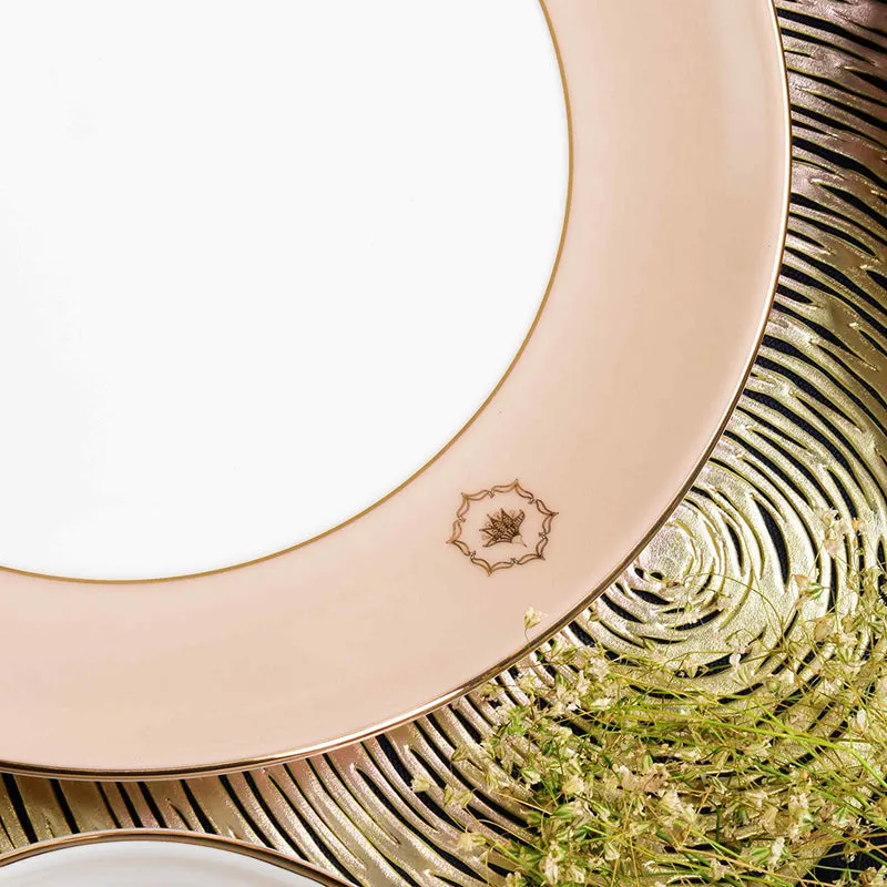 Close-up of a peach porcelain plate with gold trim and decorative centre motif