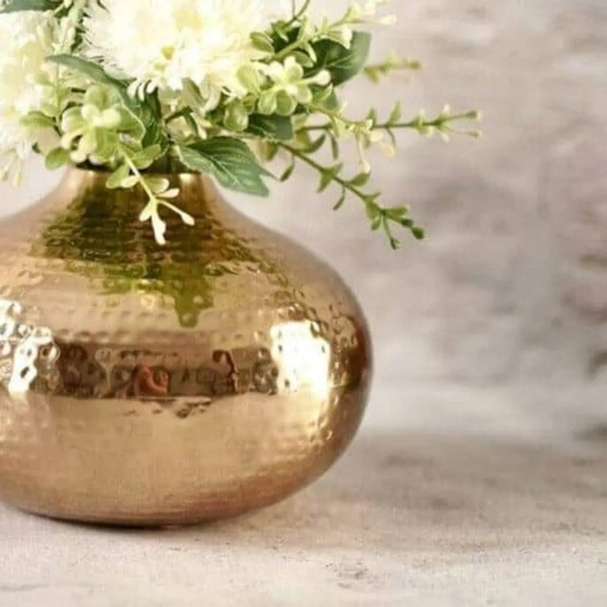 Close-up of the vase's rounded gold hammered finish with white and green flowers