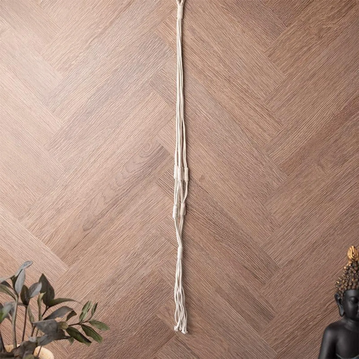 White macrame planter hanger displayed vertically against a wood-look wall