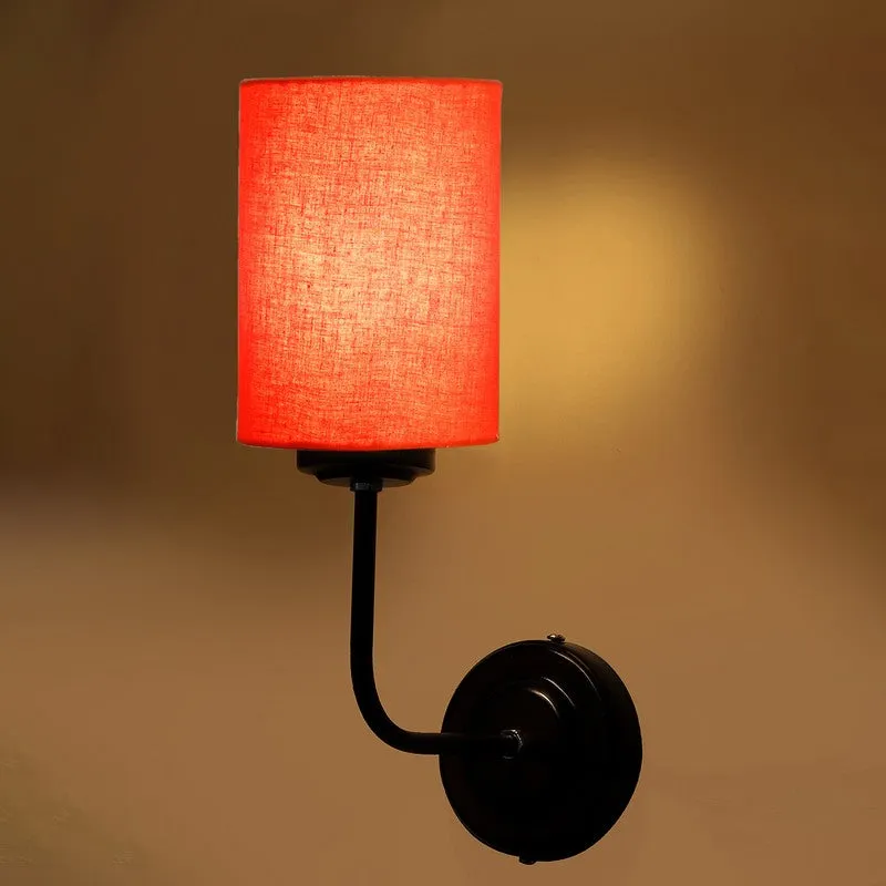 Lit orange wall lamp with cylindrical shade and black iron base