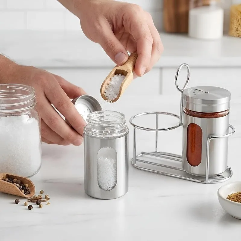 A hand fills a silver spice jar beside its matching stand.