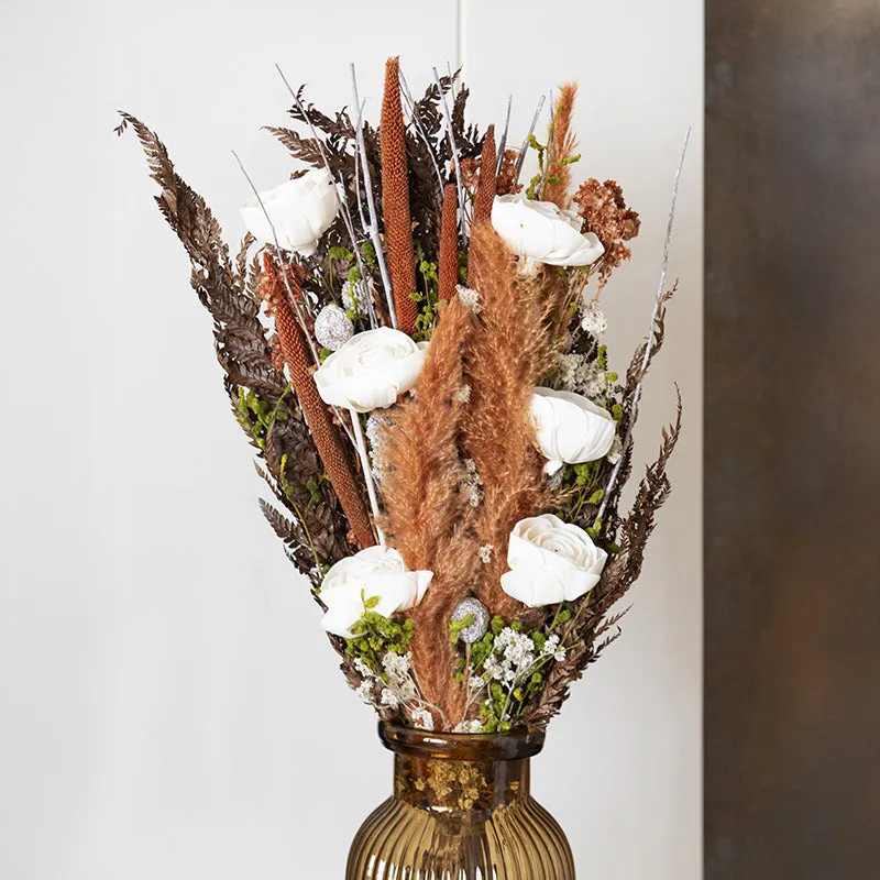 Tall dried bouquet with white flowers and earthy foliage in an amber ribbed vase