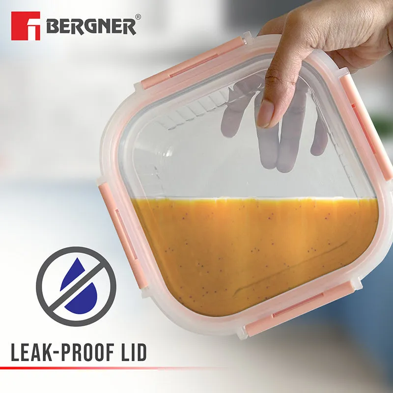 Glass lunch box tilted with orange soup inside and its peach lid secured.