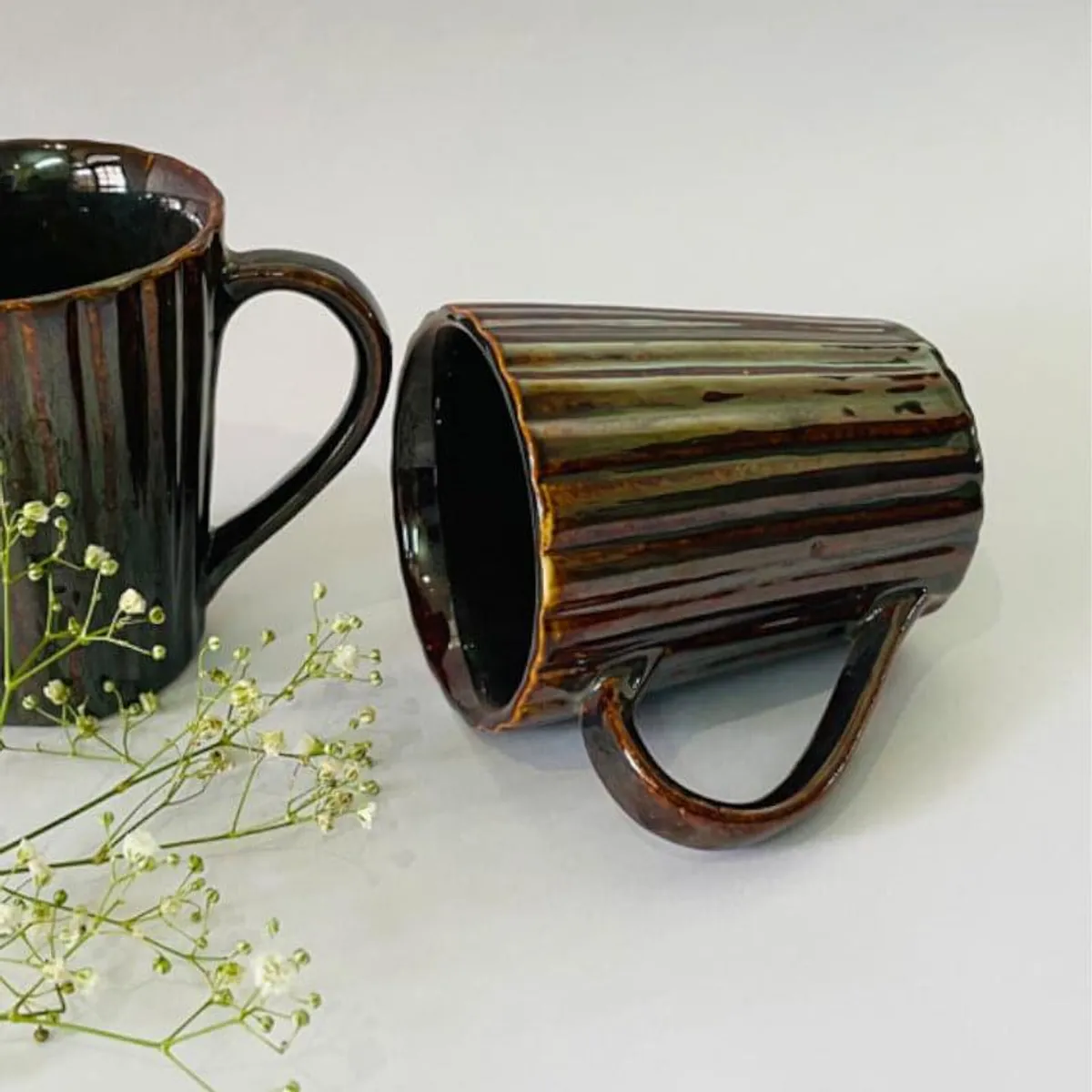 Two glossy brown ribbed ceramic mugs, one upright and one lying on its side