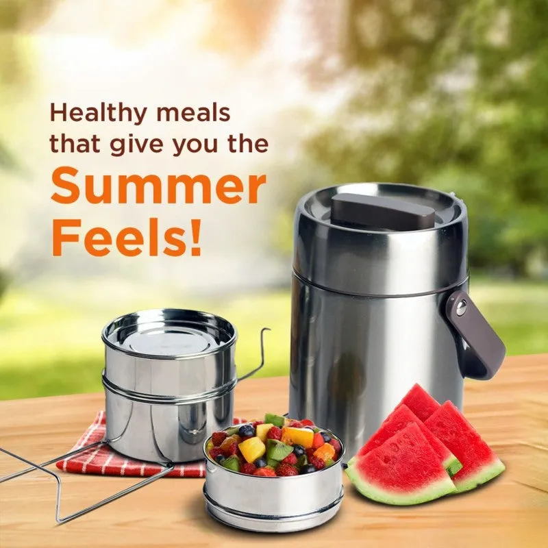 Silver three-tier tiffin carrier with stacked food containers, fruit and flatbreads outdoors