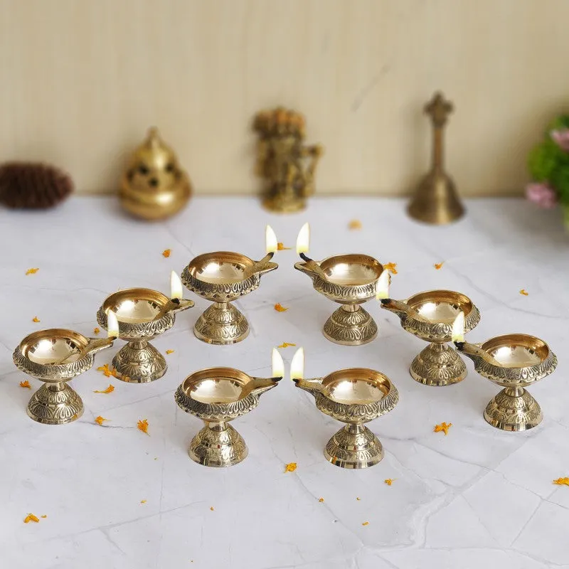 Eight gold brass diyas arranged in a circle on a light surface, with lit wicks.