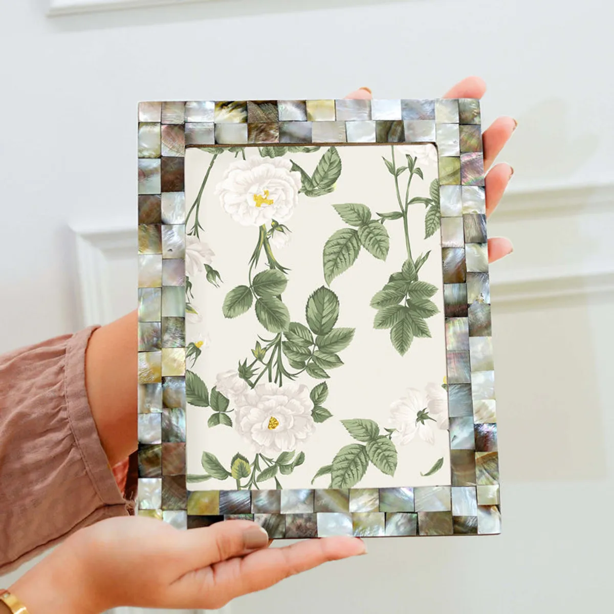 Mother-of-pearl photo frame held upright in hands against a light background.