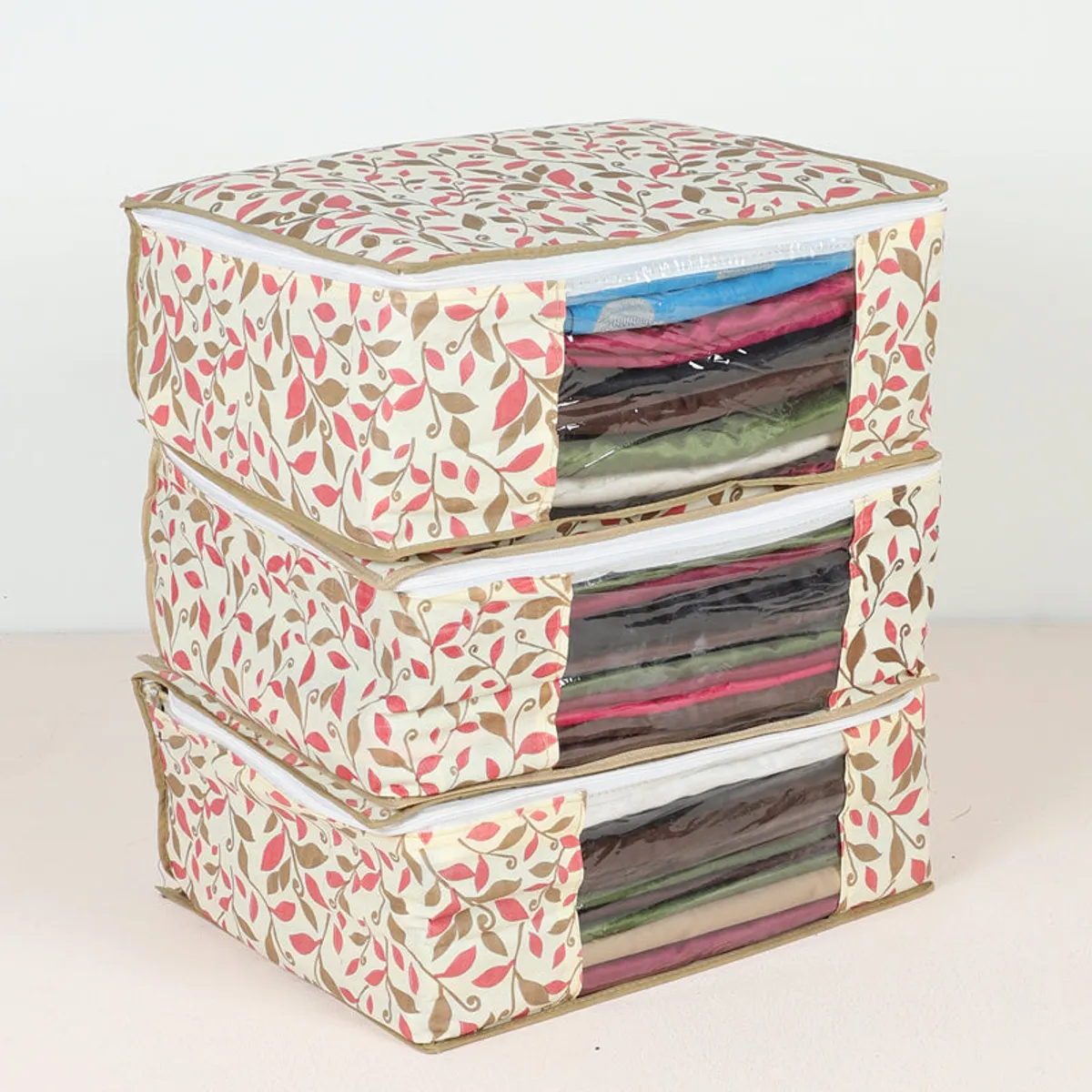 Three stacked cream cloth saree organisers with multicolour leaf pattern and clear fronts