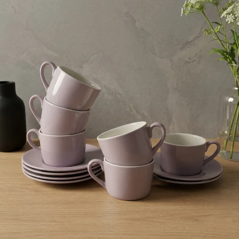 Six light purple cups and saucers arranged on a wooden table