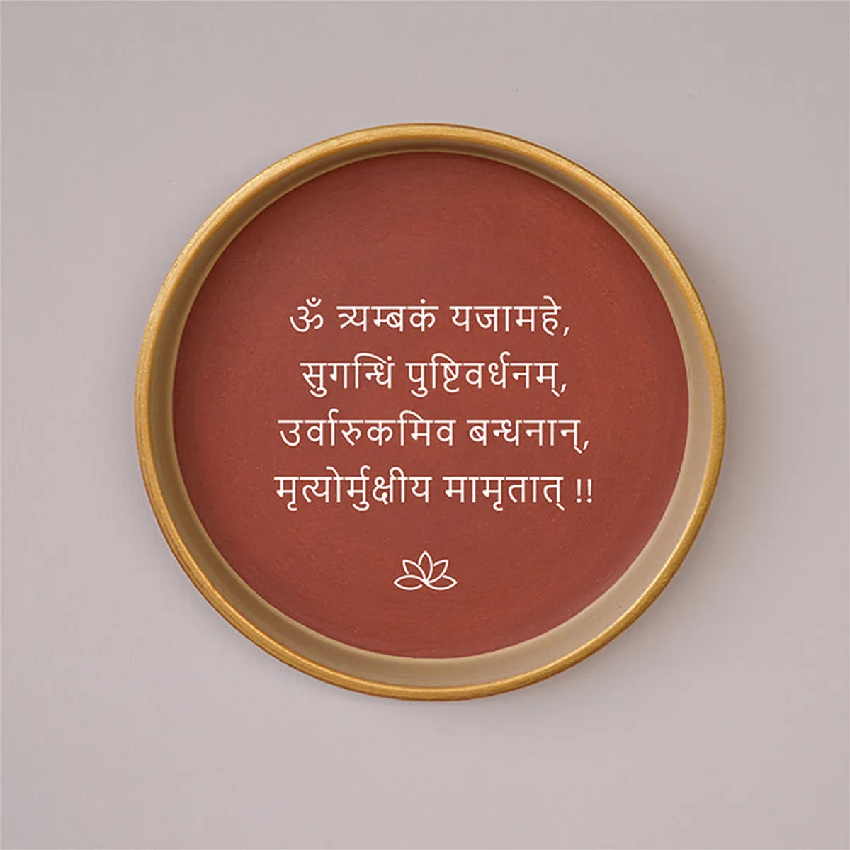 Close-up of a round terracotta wall plate with white Sanskrit script and lotus motif