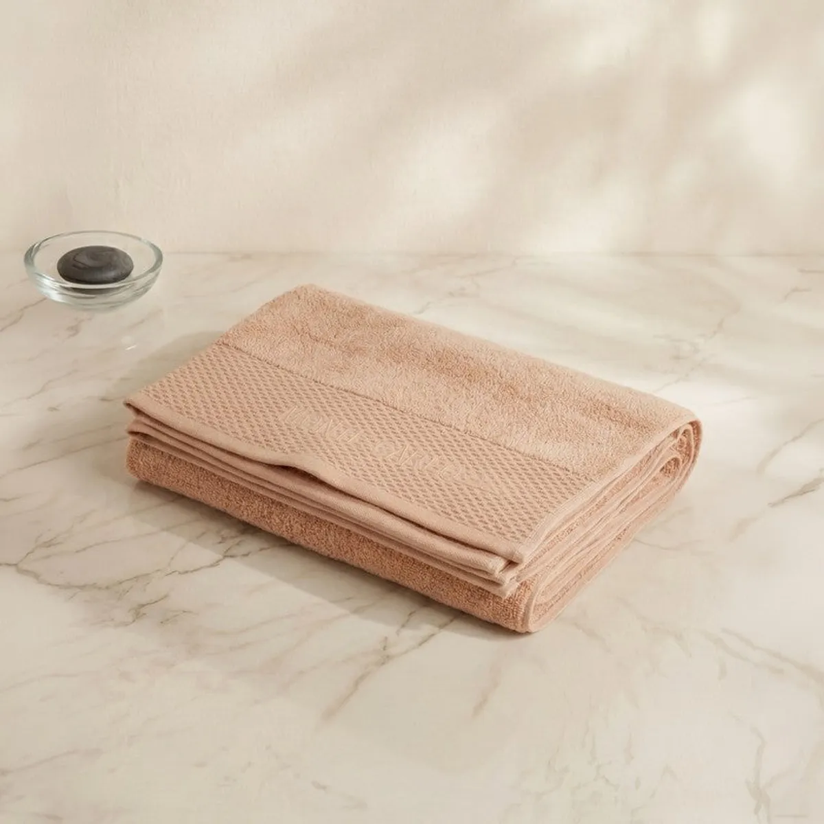 Folded dark beige bath towel displayed on a light marble surface