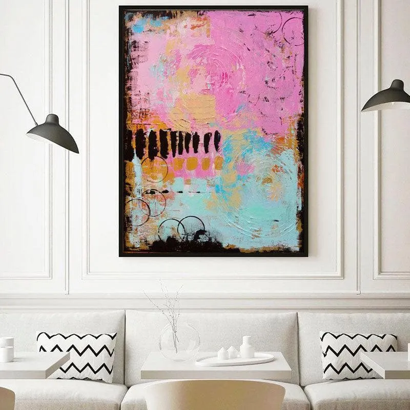 Black-framed abstract pink and blue painting displayed above a white sofa