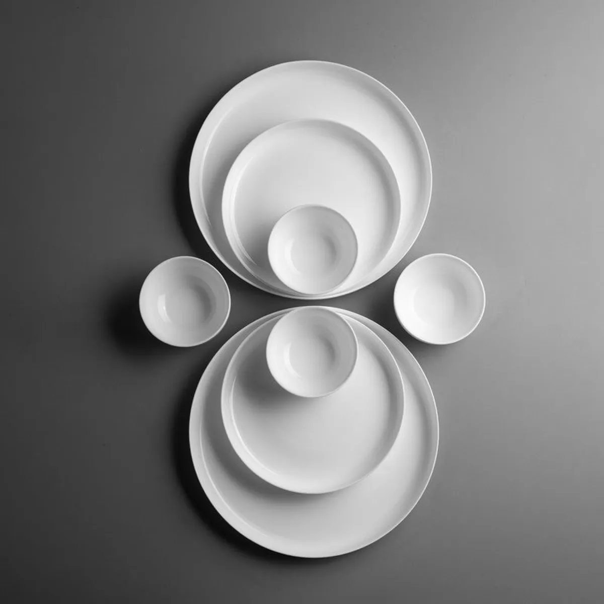 Top view of white plates and bowls arranged on a dark background