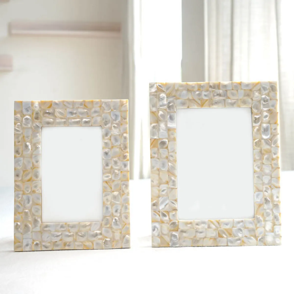 Two empty ivory pearl-mosaic photo frames standing beside a bright window.