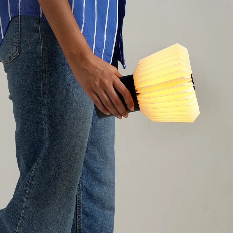 Person holding the portable glowing pleated table lamp by its black base