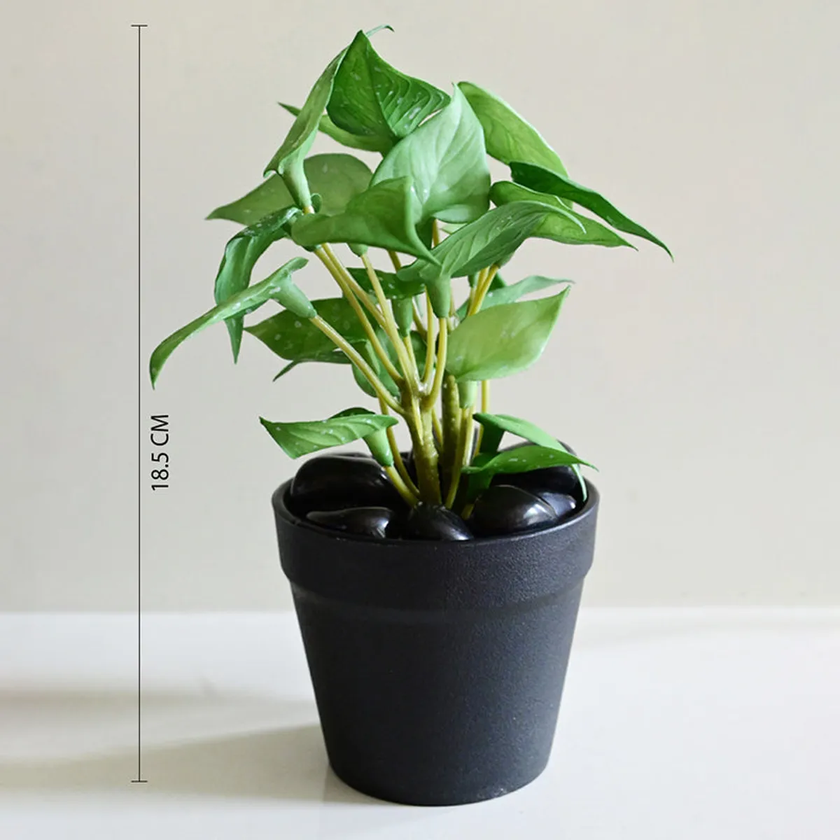 Green artificial pothos plant shown in a black pot against a plain background