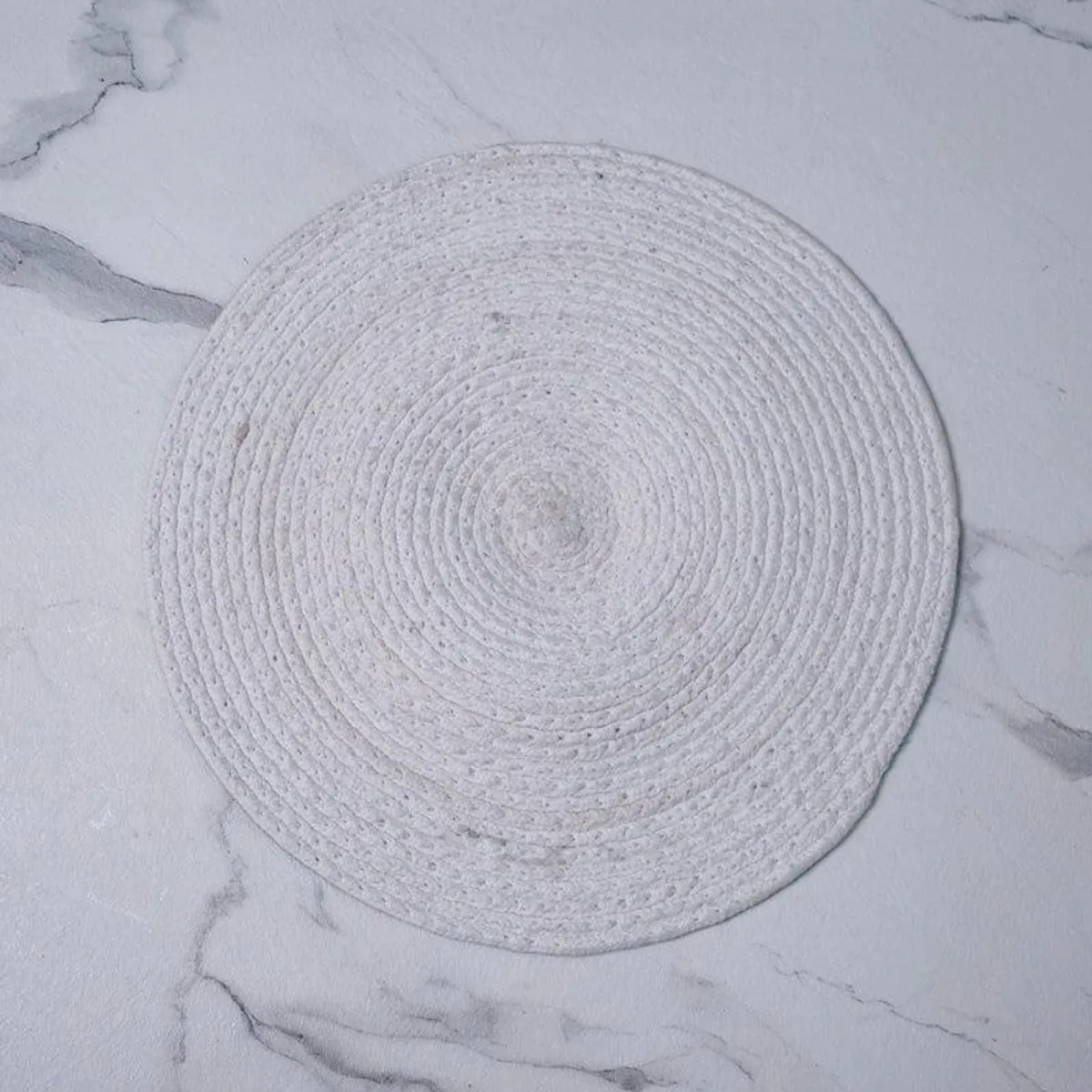 Pale textured round mat shown from the reverse side on a marble surface
