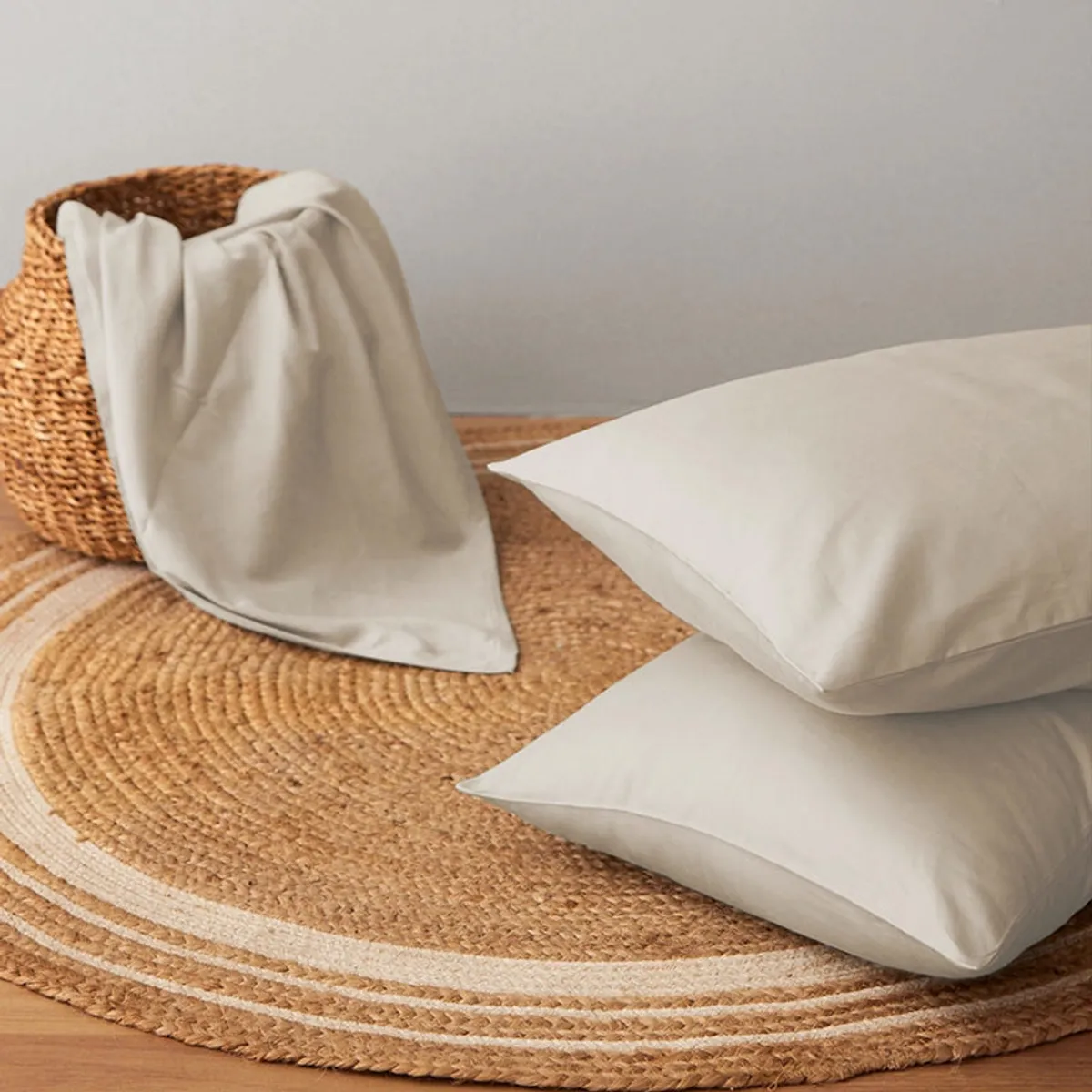 Beige sheet and pillow cover arranged on a woven basket and rug