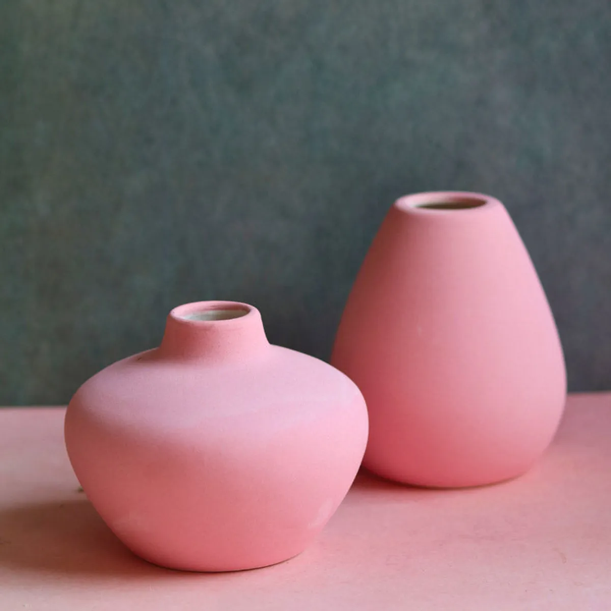Two pink ceramic vases with rounded urn-like shapes on a pink surface