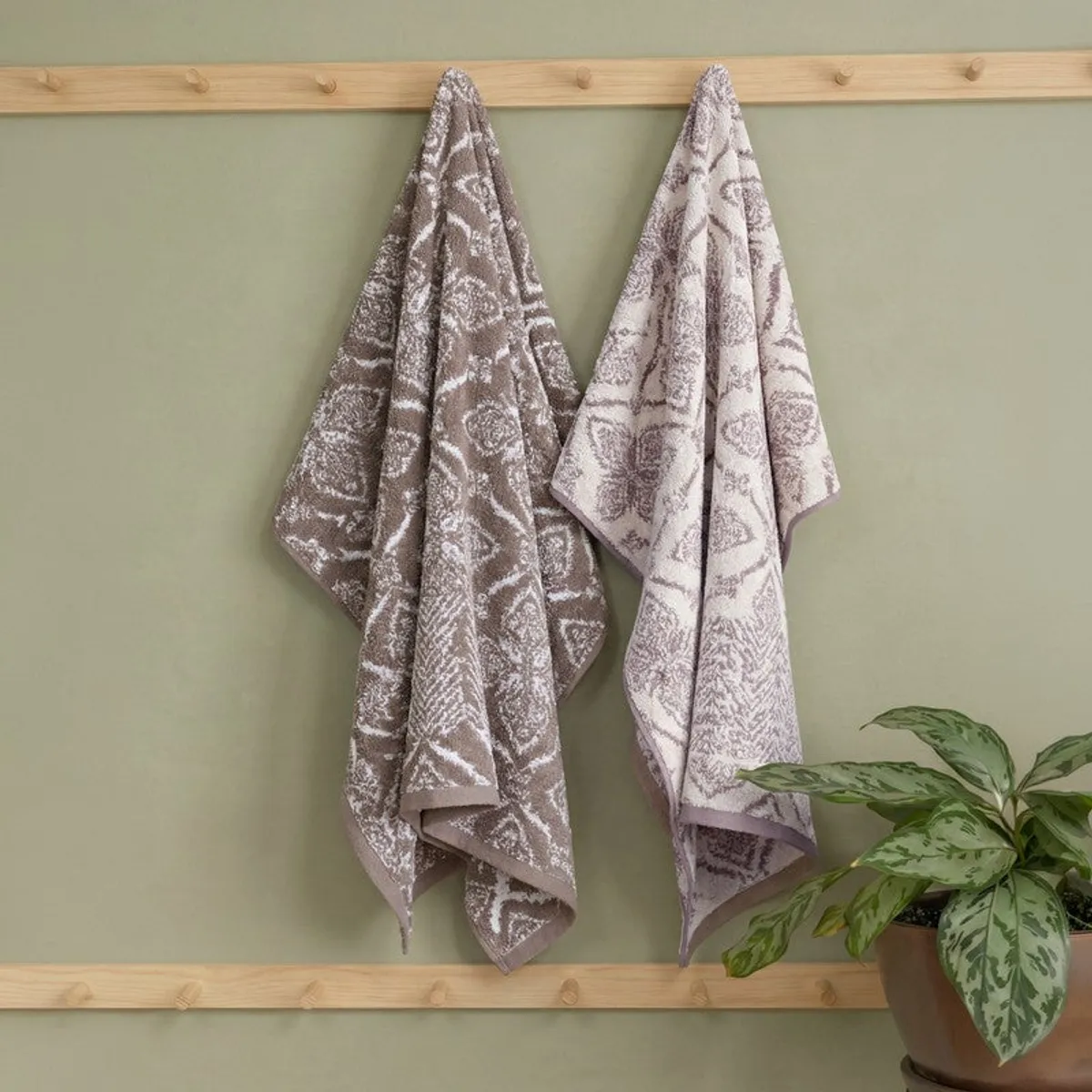 Beige floral bath towel hanging on a wooden bathroom rack beside a potted plant