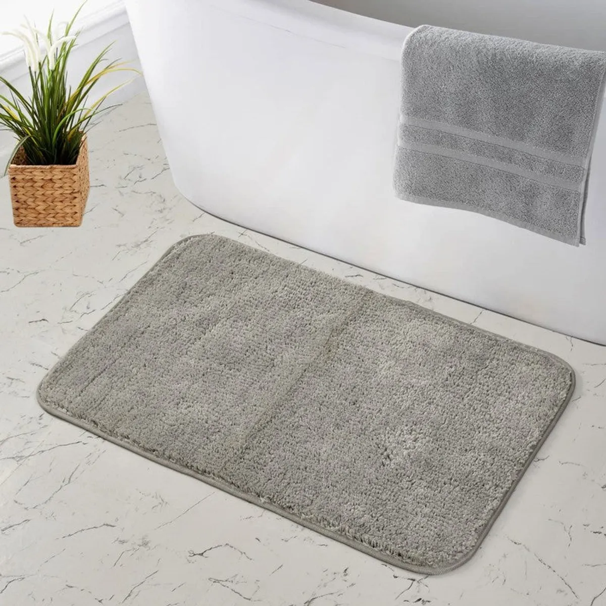 Grey rectangular bath mat beside a bathtub on a light floor