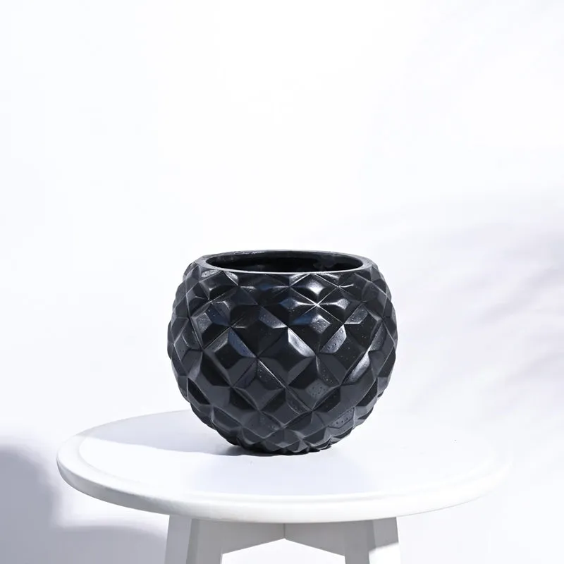 Black round planter with faceted geometric surface on a white stool