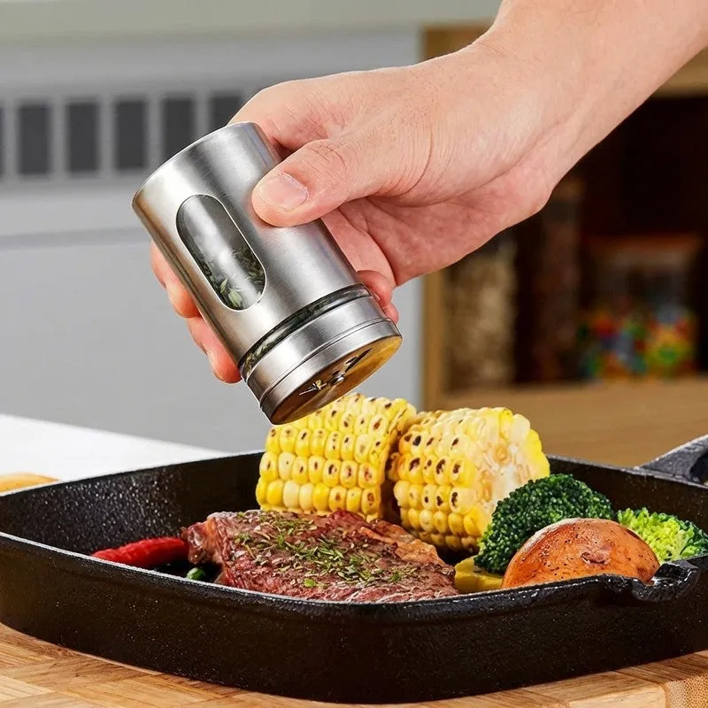 A hand uses a silver spice jar to season food in a pan.