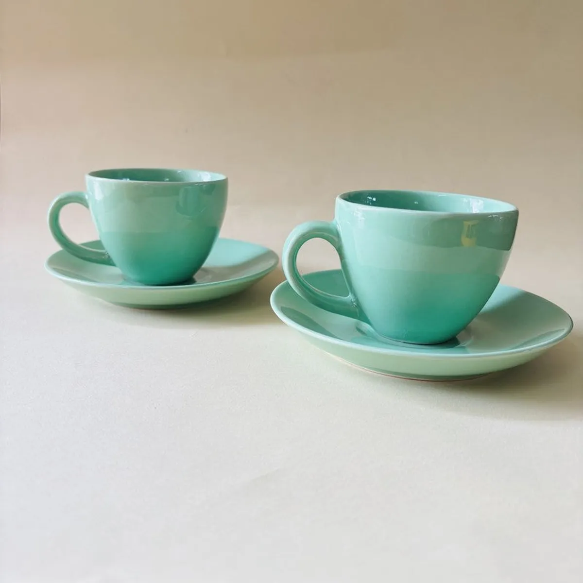 Two glossy green cup and saucer sets displayed on a light surface