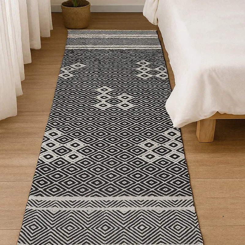 Black and off-white diamond-pattern runner rug placed beside a bed