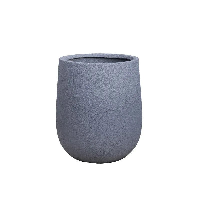 Grey planter with a leafy plant beside a lamp and curtains