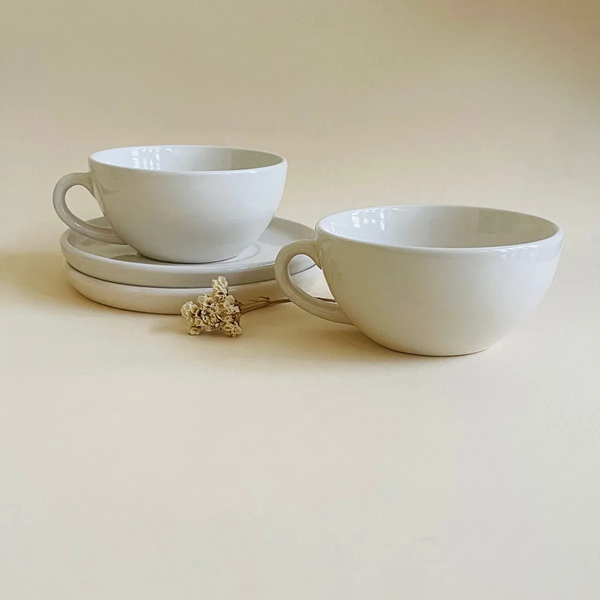 Two glossy white cups and saucers displayed against a neutral background