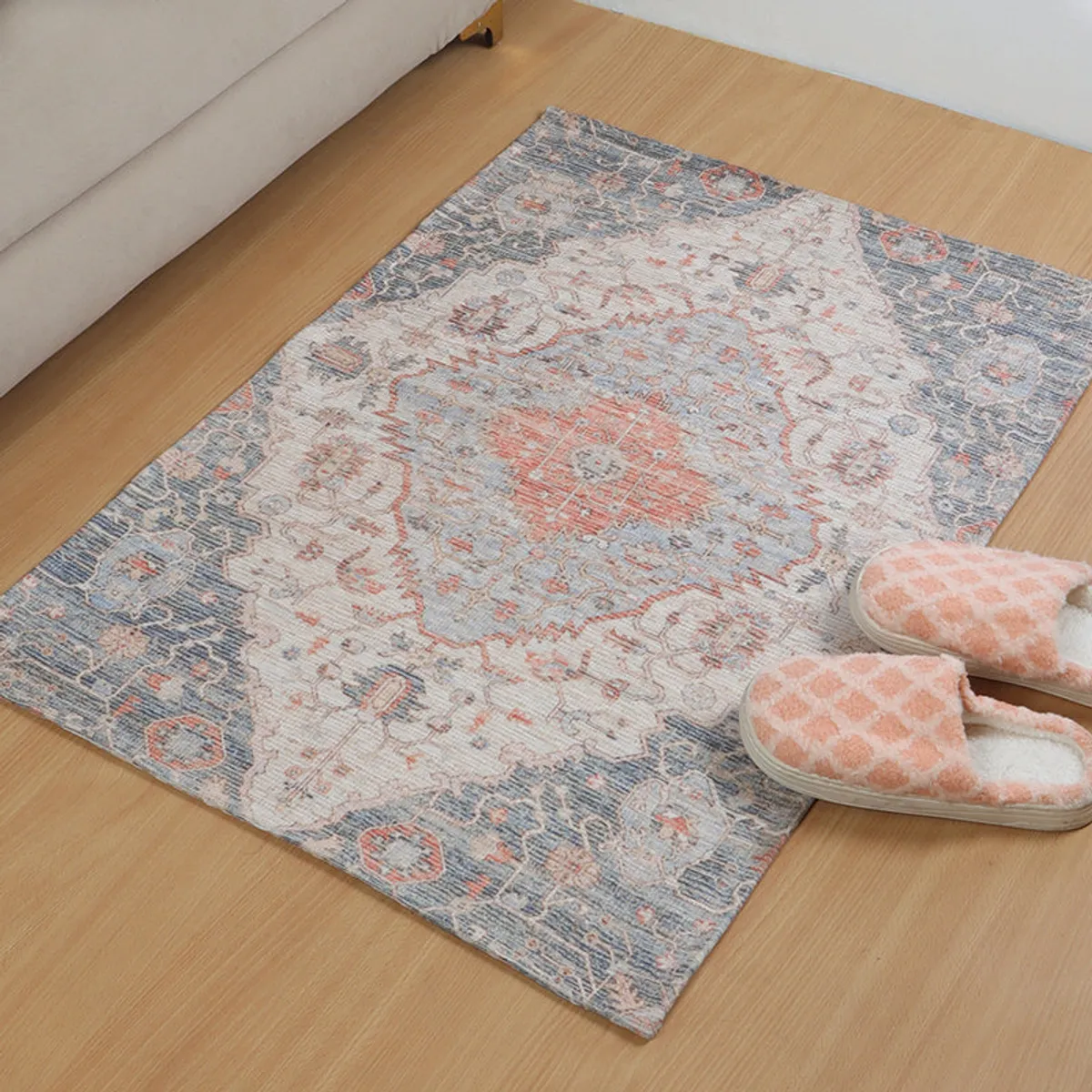 Close angled view of a beige and blue patterned doormat on a wooden floor