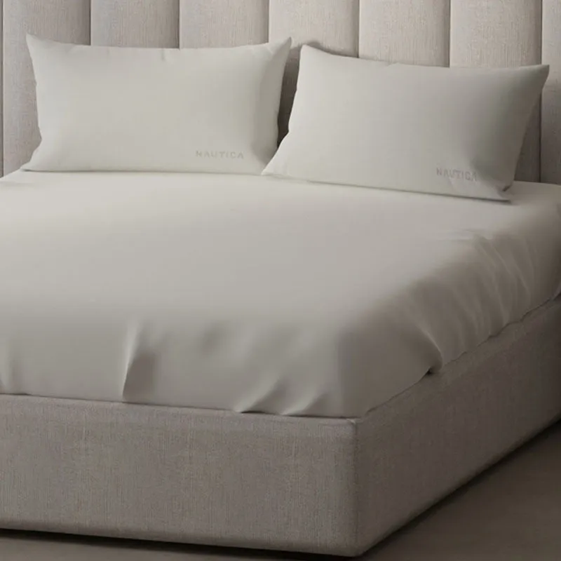 Angled close view of the off white flat bedsheet on an upholstered bed