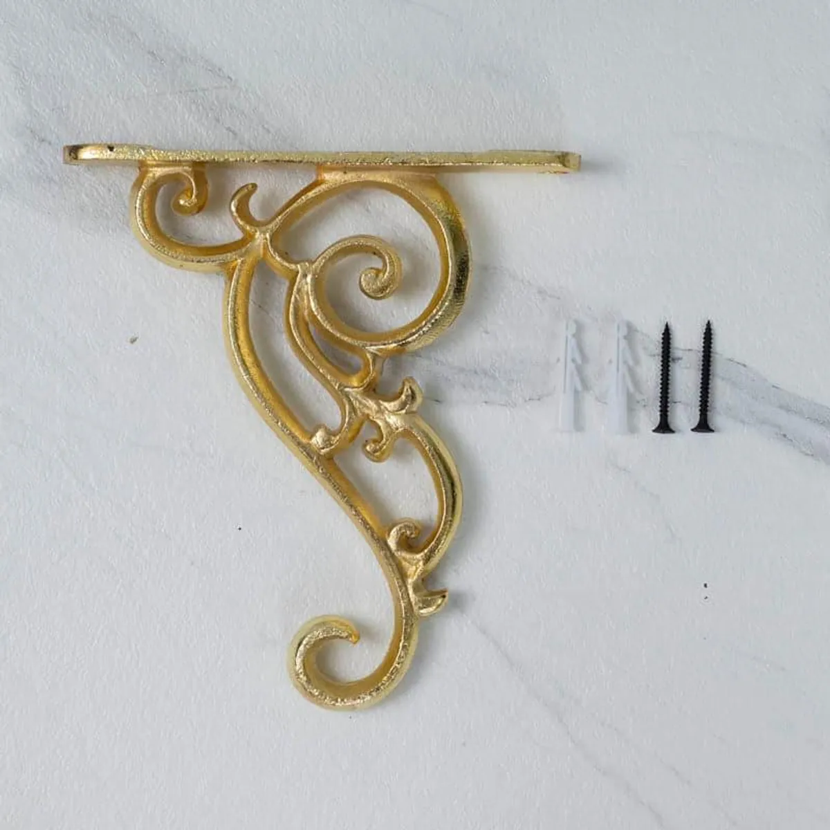 Gold ornate wall bracket shown against a white wall with two screws nearby