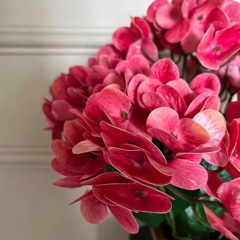 Close-up of pink artificial hydrangea-style flower petals and green leaves.