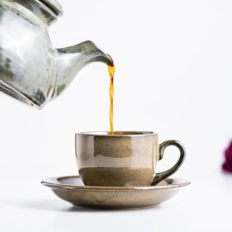Green glazed ceramic teapot pouring tea into a cup and saucer