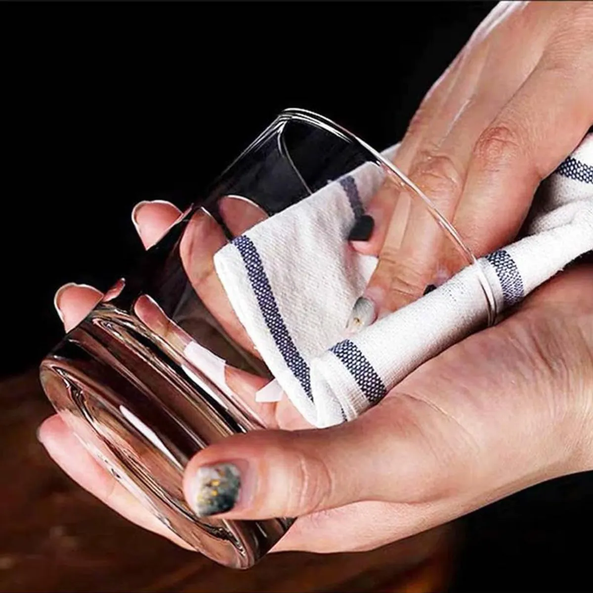 Hand drying a clear glass tumbler with a white striped cloth
