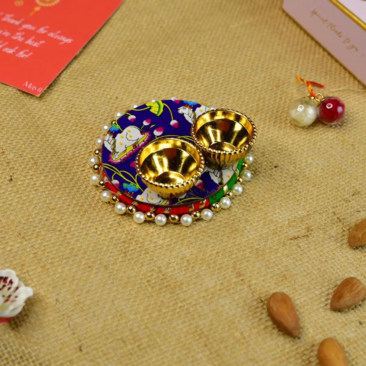 Decorated roli thali with two gold bowls and a colourful patterned base.