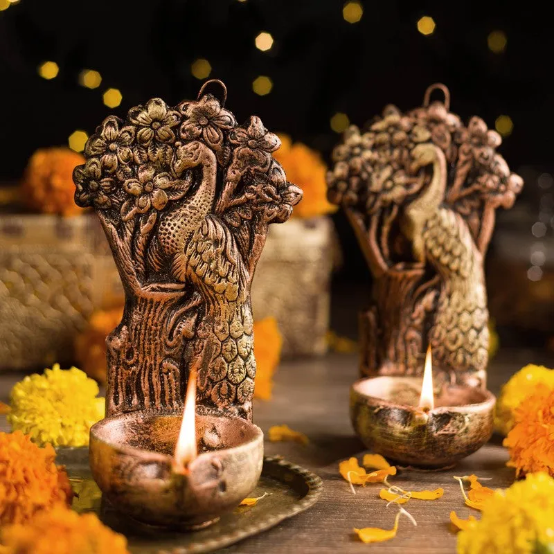 Peacock diya pair glowing with lit flames against a festive floral setting
