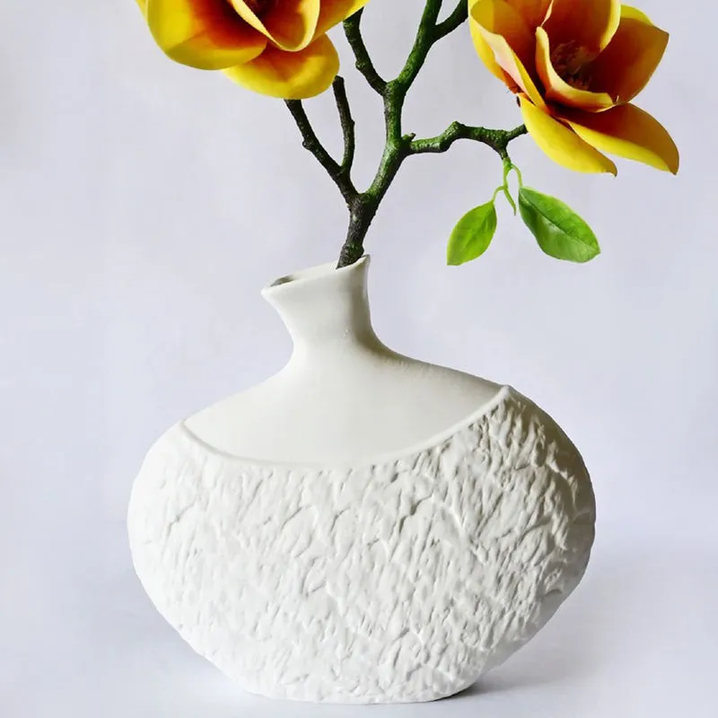 White textured vase styled with yellow flowers against a plain background.