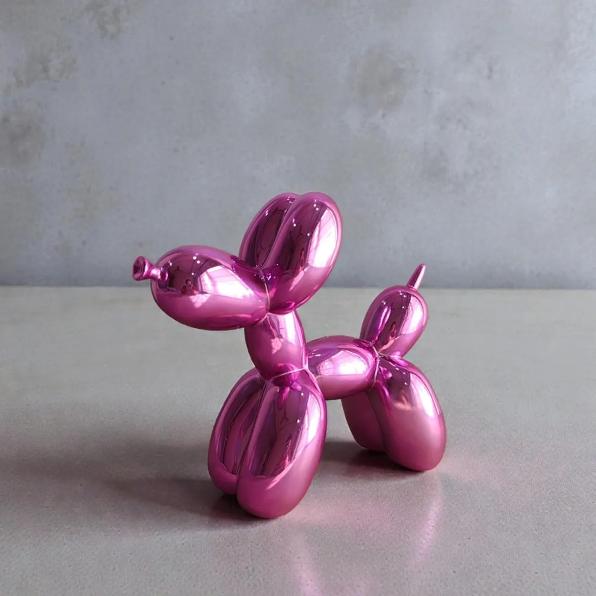 Side view of a glossy pink balloon dog showpiece on a grey surface.